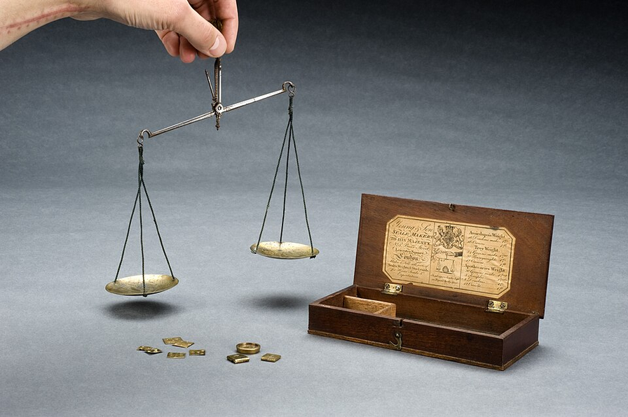 손에 든 앤티크 양팔 저울과 작은 분동 사진으로, 롱 계좌 수와 숏 자금 규모가 서로 균형을 이루는 원리를 표현한 이미지